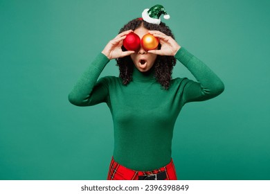 Merry little kid teen girl wearing hat casual clothes posing hold in hand cover eyes with two Christmas tree toys balls isolated on plain green background. Happy New Year celebration holiday concept - Shutterstock ID 2396398849