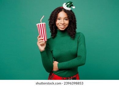 Merry little kid teen girl wear hat casual clothes posing hold in hand cup of soda pop cola fizzy water isolated on plain green background studio. Happy New Year celebration Christmas holiday concept - Shutterstock ID 2396398853