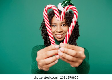 Merry little kid teen girl wear hat casual clothes posing hold in hand candy cane sticks in heart shape isolated on plain green background studio. Happy New Year celebration Christmas holiday concept - Shutterstock ID 2396398855