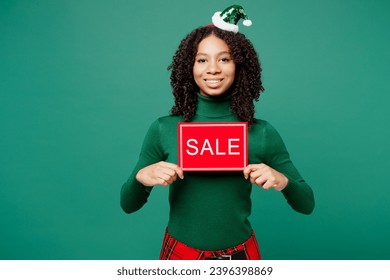 Merry little kid teen girl wear hat casual clothes posing hold in hand card sign with sale title text isolated on plain green background studio. Happy New Year celebration Christmas holiday concept - Shutterstock ID 2396398869