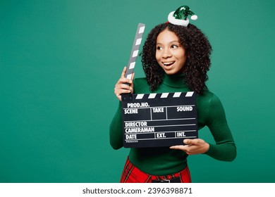 Merry little kid teen girl wears hat casual clothes posing hold classic black film making clapperboard look aside isolated on plain green background studio. Happy New Year Christmas holiday concept - Shutterstock ID 2396398871