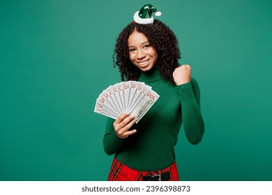 Merry little kid teen girl wear hat casual clothes posing hold fan money in dollar banknotes do winner gesture isolated on plain green background. Happy New Year celebration Christmas holiday concept - Shutterstock ID 2396398873
