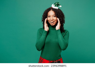Merry little kid teen girl wear turtleneck hat casual clothes posing sharing hot news about sales discount hands near mouth isolated on plain green background studio. Happy New Year holiday concept - Shutterstock ID 2396398891