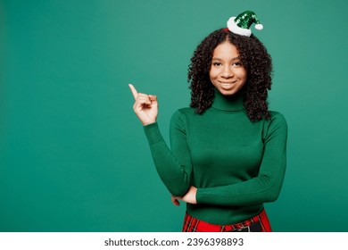 Merry little kid teen girl wear turtleneck hat casual clothes posing point index finger indicate on area copy space mock up isolated on plain green background studio. Happy New Year holiday concept - Shutterstock ID 2396398893