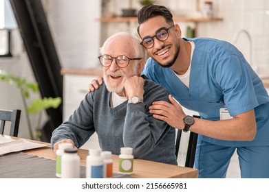 Merry Male Nurse Hugging A Pensioner In The Kitchen