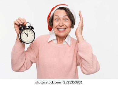 Merry minded elderly old woman wear pastel pink knitted sweater Santa hat posing hold in hand clock smiling look at camera isolated on white background. Happy New Year Christmas concept - Powered by Shutterstock