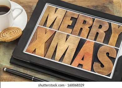 Merry Xmas in letterpress wood type on digital tablet computer with stylus pen, coffee cup and cookie