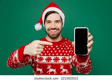 Merry young man wear red knitted sweater Santa hat posing use point finger on blank screen mobile cell phone isolated on plain dark green background studio. New Year 2023 holiday celebration concept - Powered by Shutterstock