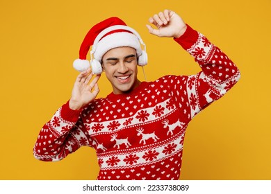 Merry young man wear red knitted christmas sweater Santa hat headphones posing listen music dance raise up hands isolated on plain yellow background. Happy New Year 2023 celebration holiday concept - Powered by Shutterstock