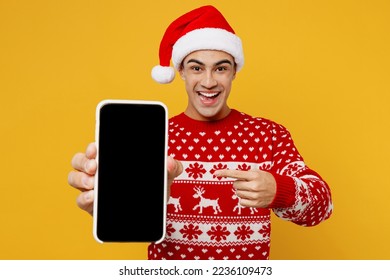 Merry young man wear red knitted christmas sweater Santa hat posing hold show use mobile cell phone blank screen workspace area isolated on plain yellow background. Happy New Year 2023 holiday concept - Powered by Shutterstock