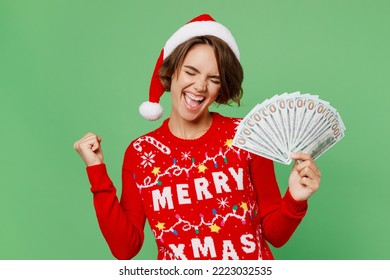 Merry young woman wear knitted xmas sweater Santa hat posing hold fan cash money dollar banknotes do winner gesture isolated on plain pastel light green background Happy New Year 2023 holiday concept