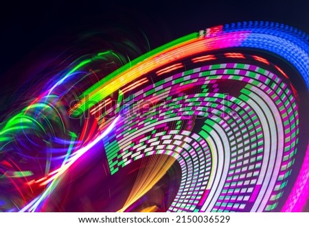 Merry-go-round carousel at night with many colorful LED light circles. Long time exposure that leaves abstract circular moving light traces and paintings on a funfair in Germany. Joyride from below.