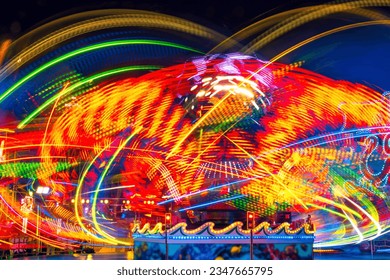 Merry-go-round at night with many colorful LED light traces. Long time exposure that leaves abstract circular moving light lines and paintings on a funfair in Germany. Turning joyride or carousel.