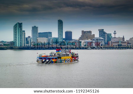 Mersey ferryboat Snowdrop, painted with Sir Peter Blake's Everybody Razzle Dazzle design, sails from Birkenhead towards Liverpool Pier Head, UK. In the distance is the famous Liverpool skyline.