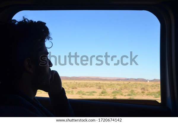 Merzouga/Morocco_04 apr\
2020: Side profile of a Caucasian man looking out the desert view\
from the open car\
window.