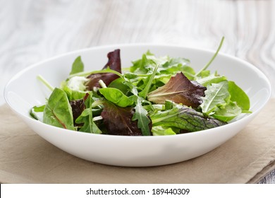 Mesclun Mix Salad In White Bowl On Wood Table