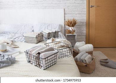 Mesh metal containers full of clothes and linen stand on the bed and on the floor in the bedroom with cup of coffee during general cleaning. Concept of updating and organizing