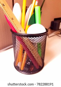 Mesh Pencil Holder Filled With Pencils, Pens, And Misc. Office Trinkets.