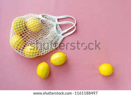 Mesh shopping bag with lemons on pink canvas background.