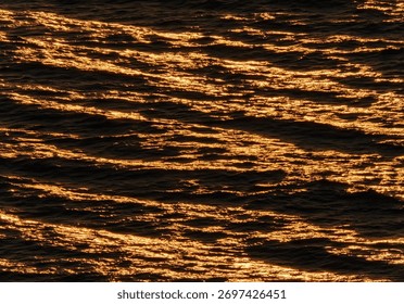 A mesmerizing abstract texture background of the deep sea surface at sunset with beautiful golden light creating a shimmering ripple pattern that looks like liquid gold