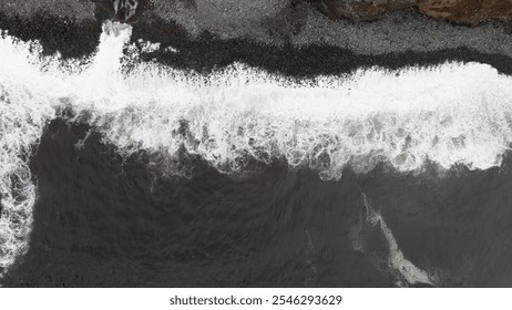 A mesmerizing aerial shot capturing the power of ocean waves crashing onto a rugged, rocky shoreline, highlighting the contrast between dark water and white foam. - Powered by Shutterstock