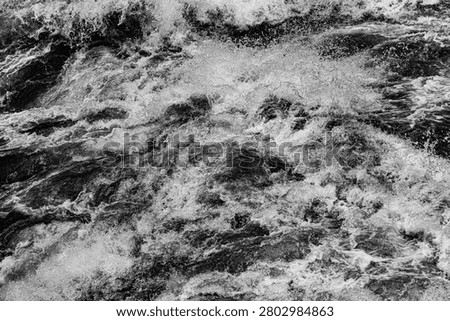 A mesmerizing black and white full-frame abstract capturing the violent, churning surface of river rapids at Tiger Leaping Gorge on the Jinsha River, China. Raging currents splinter into an aggressive, multi-directional tapestry of boiling white foam, airborne spray, and deep, dark aquatic troughs. The monochromatic presentation strips away color to emphasize raw kinetic energy, extreme surface tension, and the pure, chaotic geometry of inland river hydrology.