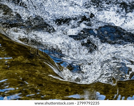 A mesmerizing close-up of crystal clear river water swirling and cascading violently over dark stones, generating bright white bubbles, foam, and dynamic natural textures.