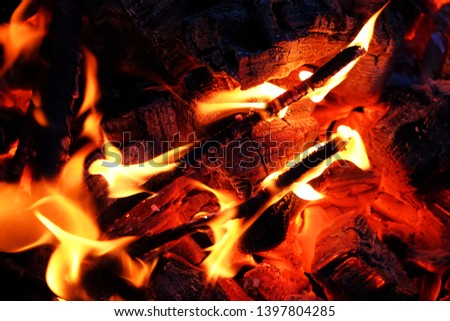 Mesmerizing closeup of small bonfire with wispy yellow orange flames totally engulfing burning branches and sticks over red hot glowing ashes and embers in bottom of round metal fire pit at night.!!