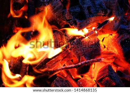 Mesmerizing closeup of small bonfire with wispy yellow orange flames totally engulfing burning branches and sticks over red hot glowing ashes and embers in bottom of round metal fire pit at night.!!