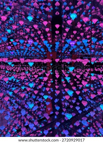 Mesmerizing immersive art installation featuring thousands of glowing pink and blue diamond shaped LED lights hanging in a mirrored room creating a surreal digital infinity effect.