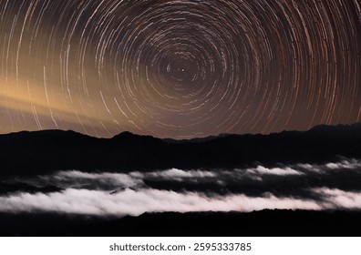 A mesmerizing long-exposure shot of circular star trails above misty mountains, blending celestial motion with the serene, cloud-covered landscape below.