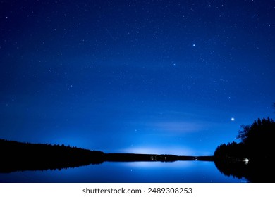 A mesmerizing starry night sky over a pond reflecting on the water surface - Powered by Shutterstock