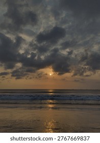 A mesmerizing sunset over the ocean with dramatic clouds and rolling waves. Golden reflections shimmer on the wet sand, creating a cinematic and tranquil seaside atmosphere.
