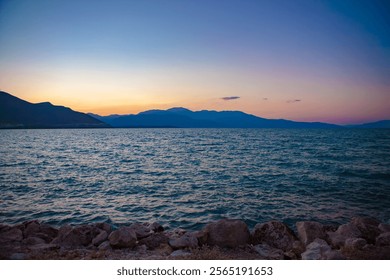 Mesmerizing sunset over a serene lake with rocky shores and distant mountains, creating a tranquil and picturesque landscape. - Powered by Shutterstock