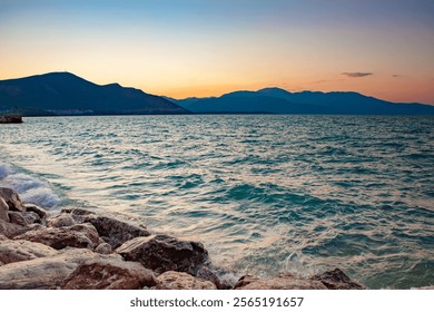 Mesmerizing sunset over a serene lake with rocky shores and distant mountains, creating a tranquil and picturesque landscape. - Powered by Shutterstock