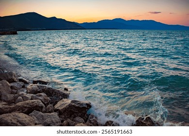 Mesmerizing sunset over a serene lake with rocky shores and distant mountains, creating a tranquil and picturesque landscape. - Powered by Shutterstock