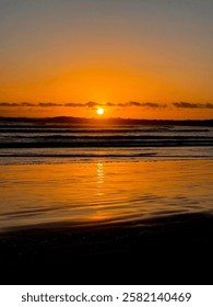A mesmerizing sunset over a tranquil beach with golden hues reflecting on the water in New Zealand