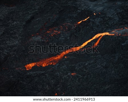 Mesmerizing view of a lava flow, red hot molten liquid streaming over black solid volcanic rocks, aerial directly above shot. Abstract, texture, and background concepts.