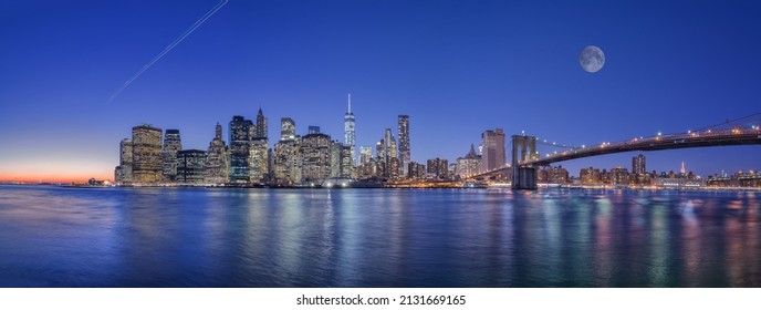 A mesmerizing view of Manhattan and Brooklyn Bridge with lights reflections in the water under moon sky, New York City