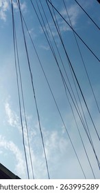 A mesmerizing view of numerous thin, dark lines diagonally intersecting a vibrant blue sky, punctuated by soft, white clouds. The lines create a dynamic, textured pattern.