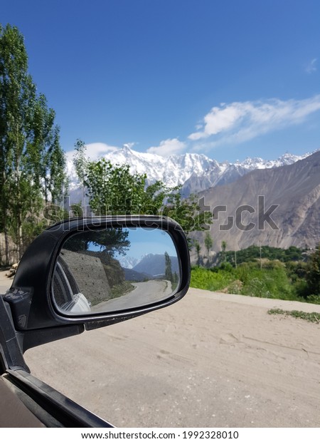 Mesmerizing view of two\
huge snow peaks at the front and back in the car mirror in Hoper\
Valley, Nagar,\
Pakistan