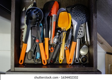 Mess in the cutlery drawer. Top view of various kitchen utensils without organization. Predominance of orange color.