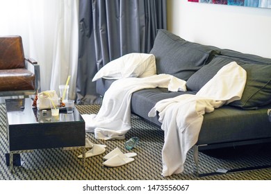 Mess In The Hotel Room. Scattered Bathrobes And Dirty And The Table With The Remnants Of Food And Plastic Cups.