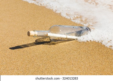 Message in a bottle washed up by the sea lying half submerged in the golden beach sand on the edge of the surf in a conceptual image of romance or a shipwreck. - Shutterstock ID 324013283