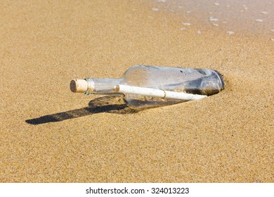 Message in a clear glass corked bottle partially buried in beach sand conceptual of a love letter from a sweetheart or plea for help form a shipwreck or marooned sailor carried ashore by the tides. - Shutterstock ID 324013223