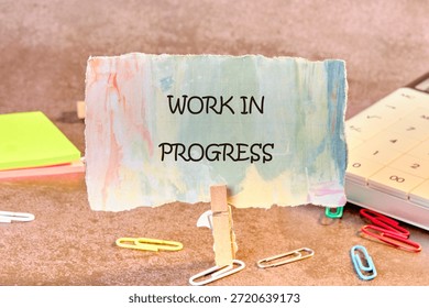 Message displays work in progress as a crafty concept. Notepads, paperclips, and calendar surround a paper message on a textured surface.