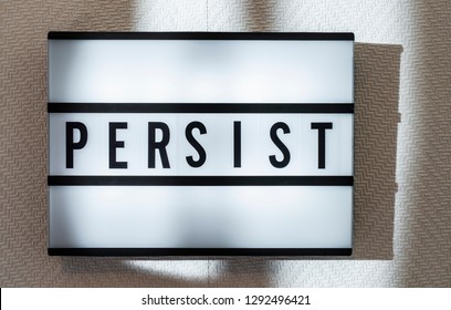 Message Persist on illuminated board. Persistence concept with text. Daylight from window. Room interior. Black letters persist on white wallpaper wall.