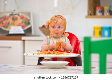 Messy Baby Boy Sits In High Chair Covered In Spaghetti And Sauce