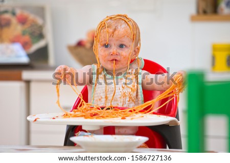 Messy Baby Boy Sits In High Chair Covered In Spaghetti And Sauce