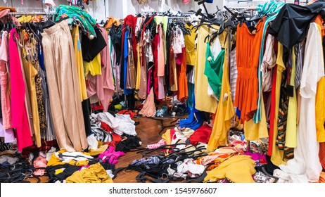 Messy clearance section in a clothing store, with colorful garments on racks and on the floor; fast fashion concept
